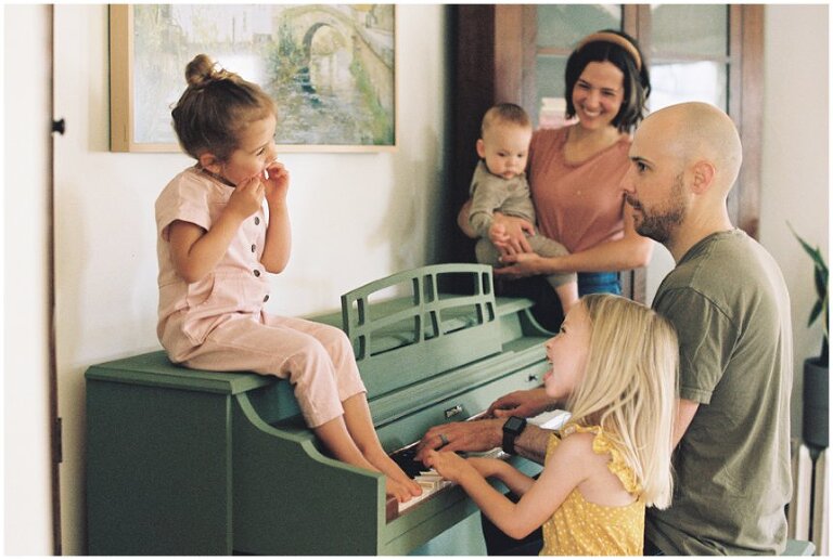 family smiling gathered around dad playing piano 