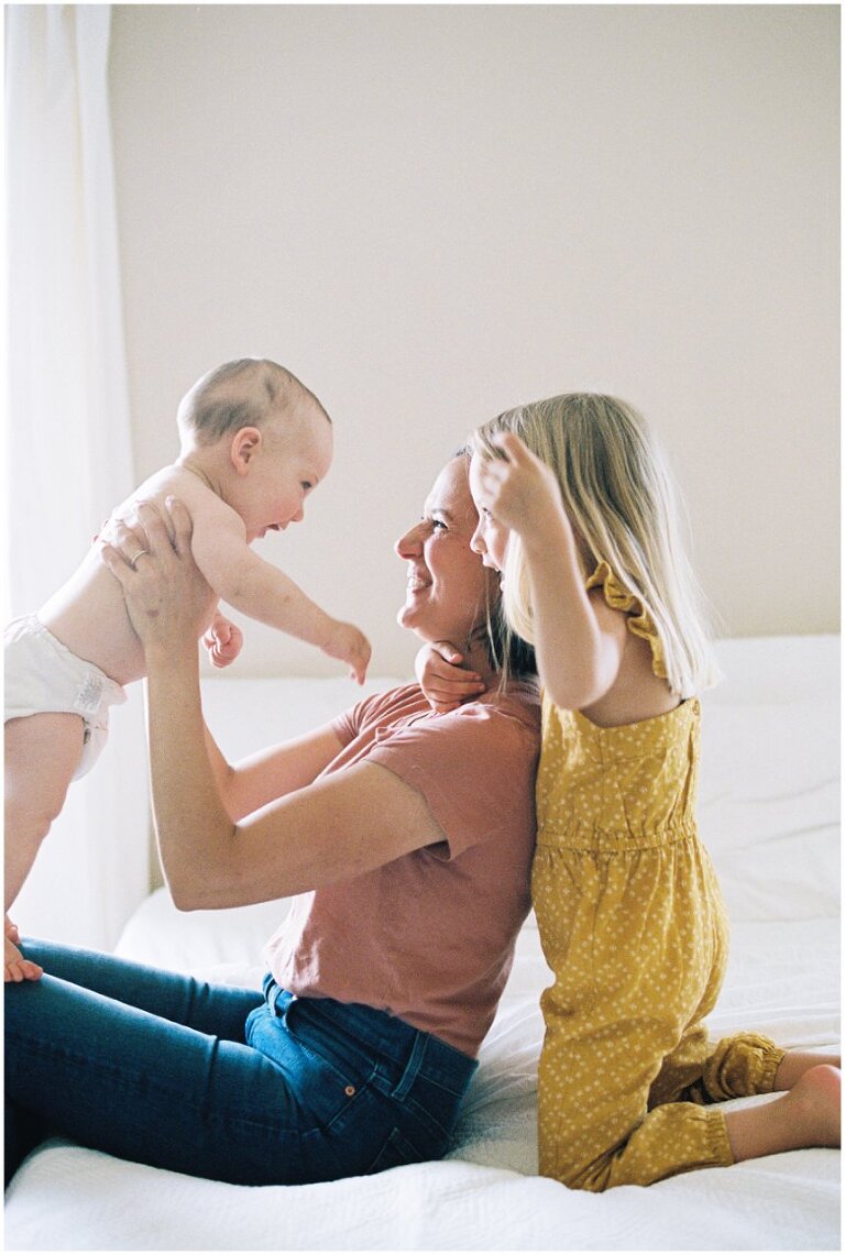 mom holding baby upright with daughter hugging from behind 