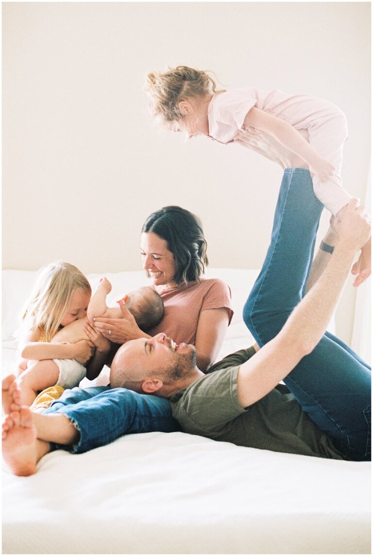 family photo playing in bed with one toddler in the air 